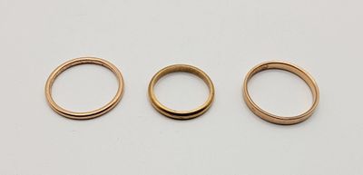 three gold wedding rings on a white surface