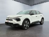Une voiture blanche est garée dans une grande pièce au sol gris.