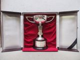 un trophée en argent dans un coffret rouge posé sur un tissu rouge