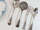 five silver spoons and two silver spoons on a white table