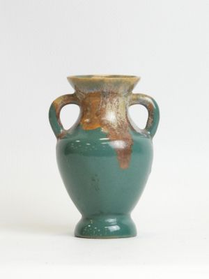 a green vase with two handles sitting on a white surface