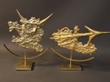 pair of gold metal sculptures of a dragon and a ship on a stand