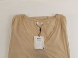 Le t-shirt est de couleur beige et comporte une étiquette.