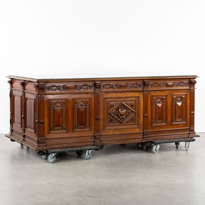 un buffet ancien en bois monté sur roulettes, orné de sculptures sur le dessus