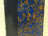 un gros plan d'un livre bleu et doré posé sur une surface blanche