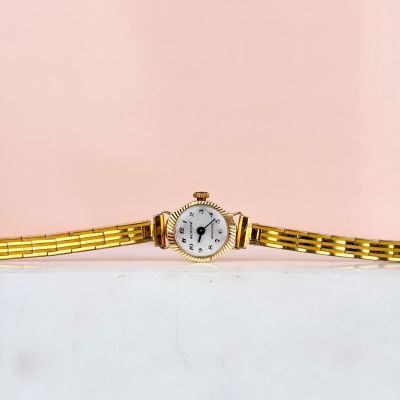 un gros plan d'une montre posée sur une surface blanche, avec un fond rose
