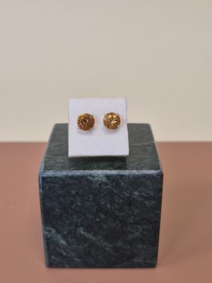 boucles d'oreilles à clous plaquées or, posées sur un socle en marbre, sur un fond rose