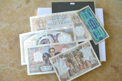 quatre billets de banque différents posés sur une table, à côté d'un passeport