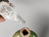 a hand that is holding a knife over a green vase