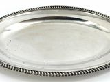 an oval silver plate with a rope edge on a white surface