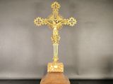 un crucifix en or posé sur un socle en bois, sur fond gris