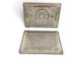 two silver trays with ornate designs on them on a white surface