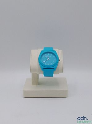 montre bleue et blanche posée sur un socle blanc, sur une surface blanche