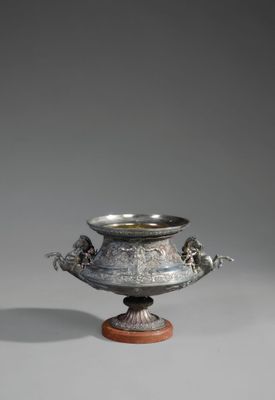 un vase en argent posé sur un socle en bois, lui-même posé sur une surface grise