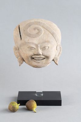 une photo représentant une sculpture représentant le visage d'un homme, posée sur un socle à côté d'un fruit