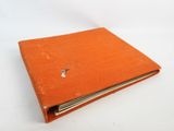 un livre orange posé sur une table blanche, près d'un mur blanc