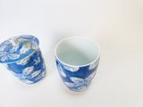 une tasse bleue et blanche avec un couvercle, à côté d'une tasse bleue et blanche décorée de feuilles