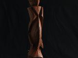 une sculpture en bois représentant une personne debout devant un fond noir
