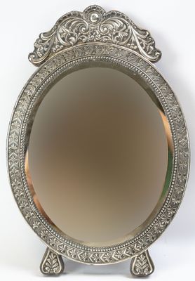 miroir plaqué argent avec un motif ouvragé, posé sur un socle, sur fond blanc