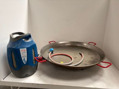 une grande poêle posée sur une étagère à côté d'un bidon bleu