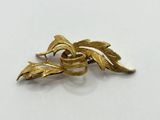 a close up of a gold leaf brooch on a white surface