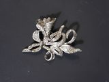 a silver brooch with a flower on it on a black surface