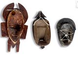 three wooden masks are lined up on a white surface