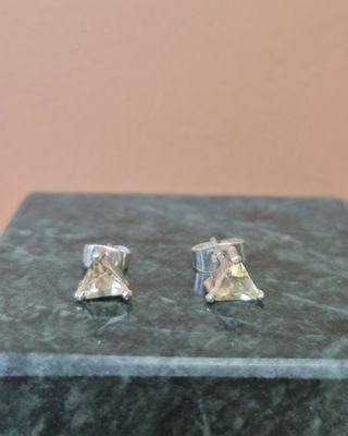 paire de boucles d'oreilles en argent ornées d'un diamant jaune, posées sur un bloc de marbre