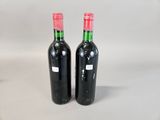 two bottles of red wine sitting next to each other on a white surface