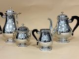 three silver coffee pots and two silver cups on a table