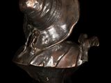 bronze bust of a woman with a hat and scarf on a black background