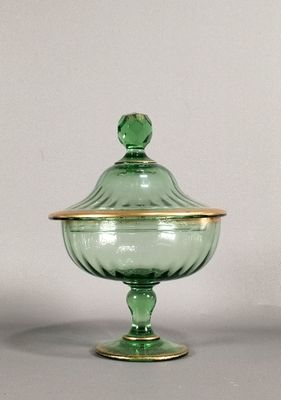 un saladier en verre vert avec un couvercle doré posé sur une table