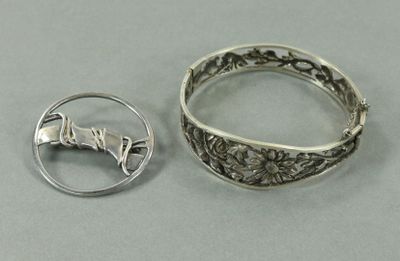 deux bagues en argent et une broche en argent posées sur une surface grise