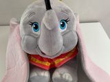 un éléphant en peluche assis sur une table blanche, sur laquelle est posé un chapeau jaune