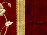 close up of a red and gold embroidered fabric with a white flower