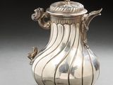 an antique silver coffee pot with a spoon on a table