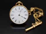 une montre de poche en or avec une clé, posée sur un fond noir