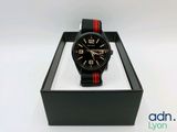 une montre noire et rouge dans un coffret noir posé sur une surface blanche