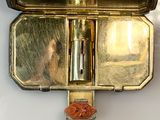 a gold case with a cigarette in it on a white surface