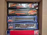 des boîtes contenant un assortiment de petits trains miniatures, rangées dans un carton posé sur une table