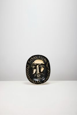 une assiette noire et dorée sur laquelle est représenté un visage