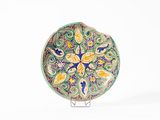 une assiette décorative posée sur un socle, sur une surface blanche