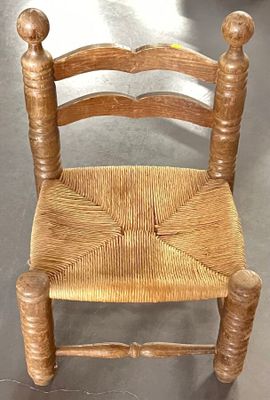 une petite chaise en bois avec une assise tressée, posée par terre