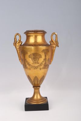 un vase doré posé sur un socle noir, sur fond blanc