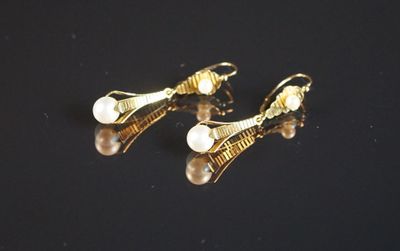 une paire de boucles d'oreilles en perles et en or posées sur un fond noir