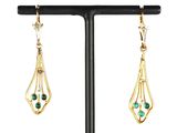 une paire de boucles d'oreilles en or et émeraude posée sur un socle noir