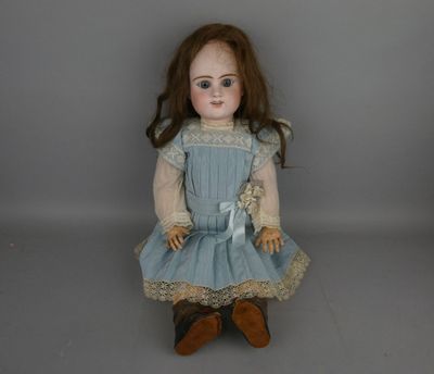 une vieille poupée vêtue d'une robe bleue et de chaussures marron, assise sur une surface grise