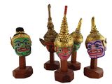 trois masques de couleurs différentes posés sur des socles en bois, sur un fond blanc