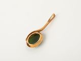 a close up of a gold spoon with a green stone in it