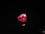 un gros plan d'un diamant rouge en forme de cœur sur une surface noire